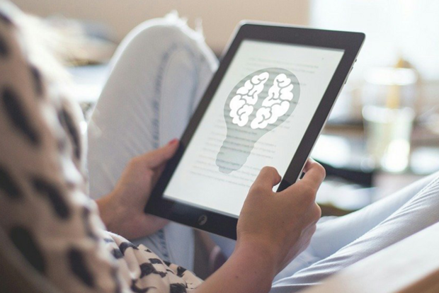 Person mit einem Tablet, auf dem eine Bildkomposition aus Gehirn und Gl&uuml;hbirne zu sehen ist